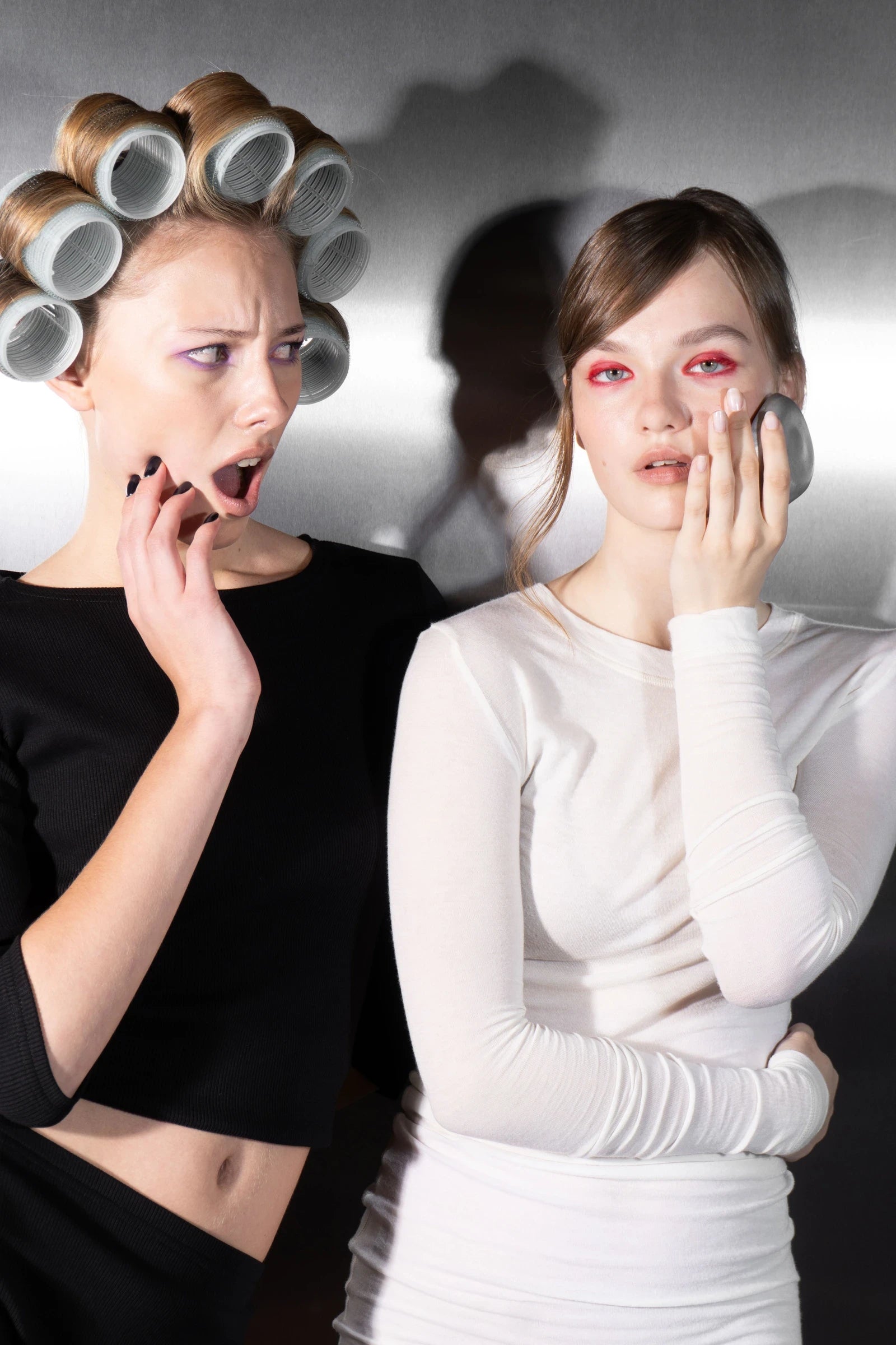 A model in hair rollers gasps beside a model in white who holds the Rhia Skin tracker to her cheek