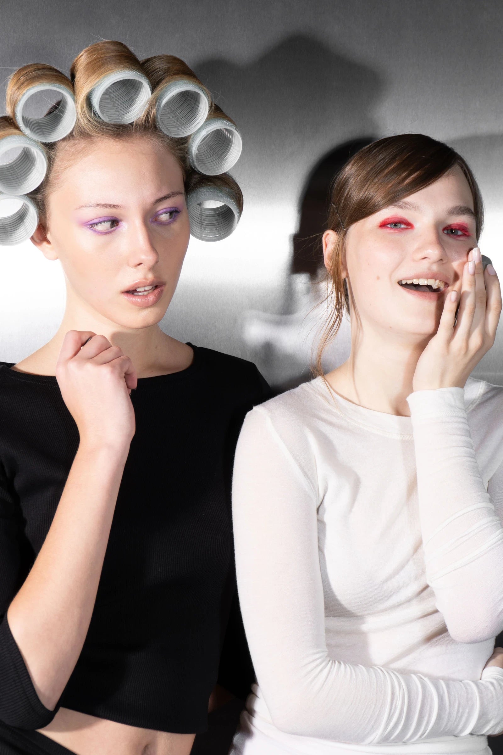 A model in white laughs with the Rhia Skin tracker at her cheek as a model in hair rollers looks on